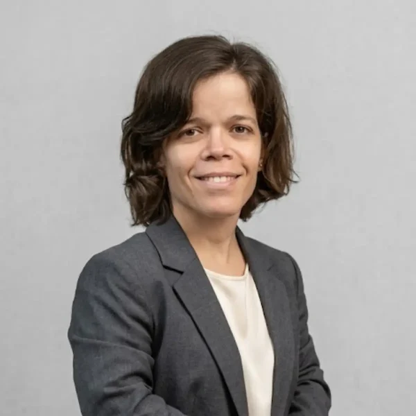 Professional headshot of a woman with short brown hair, wearing a gray blazer and white blouse, smiling against a neutral gray background.