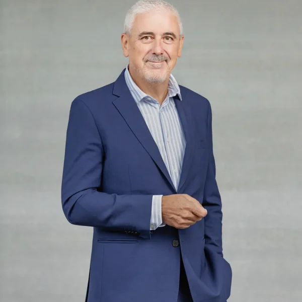 Portrait of a smiling middle-aged man in a blue suit against a gray backdrop, posing for a professional headshot.