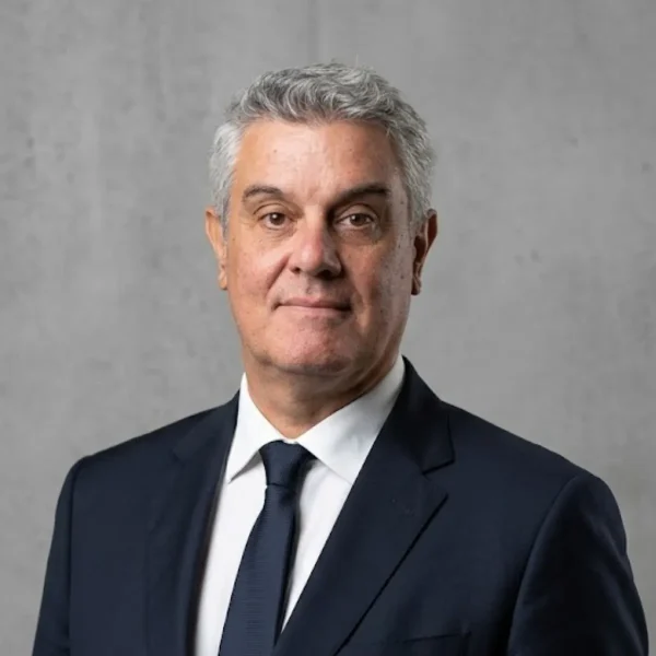 Professional headshot of a middle-aged man in a navy suit and tie against a gray backdrop.