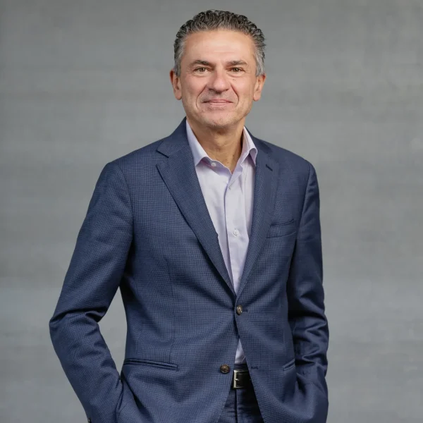 Portrait of a smiling man in a navy blue suit against a gray backdrop, professional headshot style.